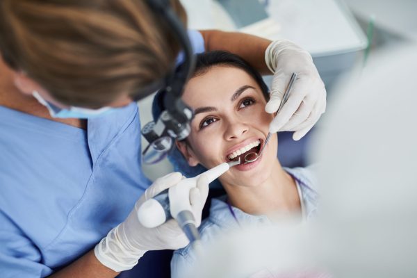 Top view portrait of beautiful lady with opened mouth sitting in dentist chair while stomatologist in sterile gloves doing professional teeth cleaning
